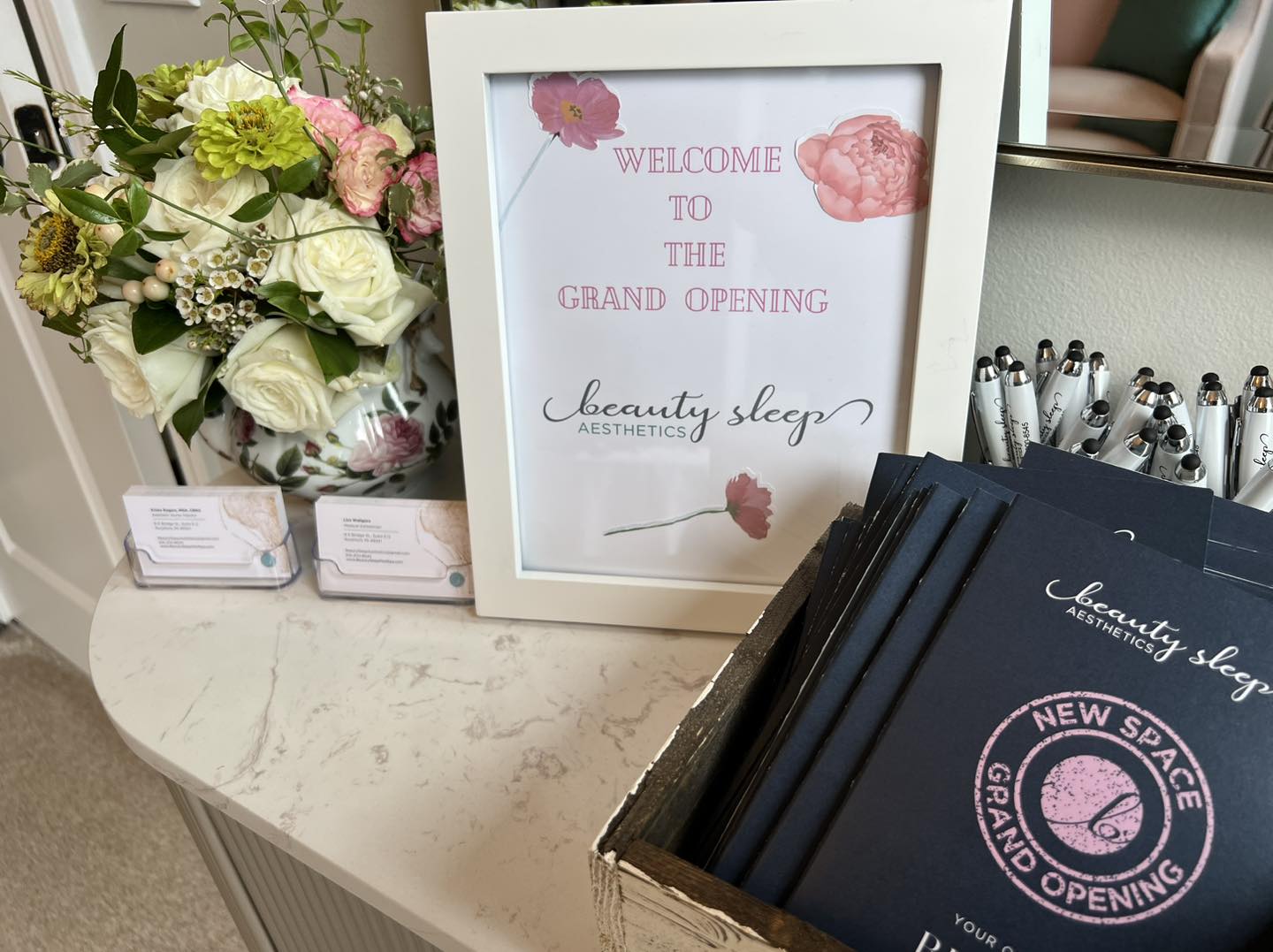 Grand-opening florals and Beauty Sleep Aesthetics branding on a marble counter